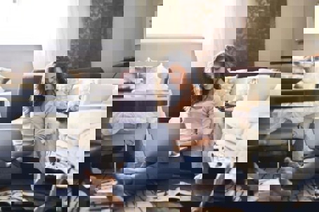 A woman sits on the floor smiling, working on a laptop