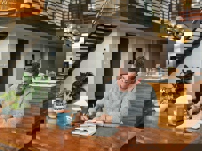 A man sits at a wooden table writing in a notebook, enjoying the comfort of his modern, well-lit home