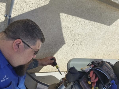 An HVAC technician uses a screwdriver on an outdoor unit near a house