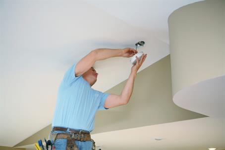 An electrician installs a ceiling light fixture