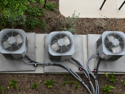 Three gray HVAC units sit on a concrete slab, connected with tubes and wiring